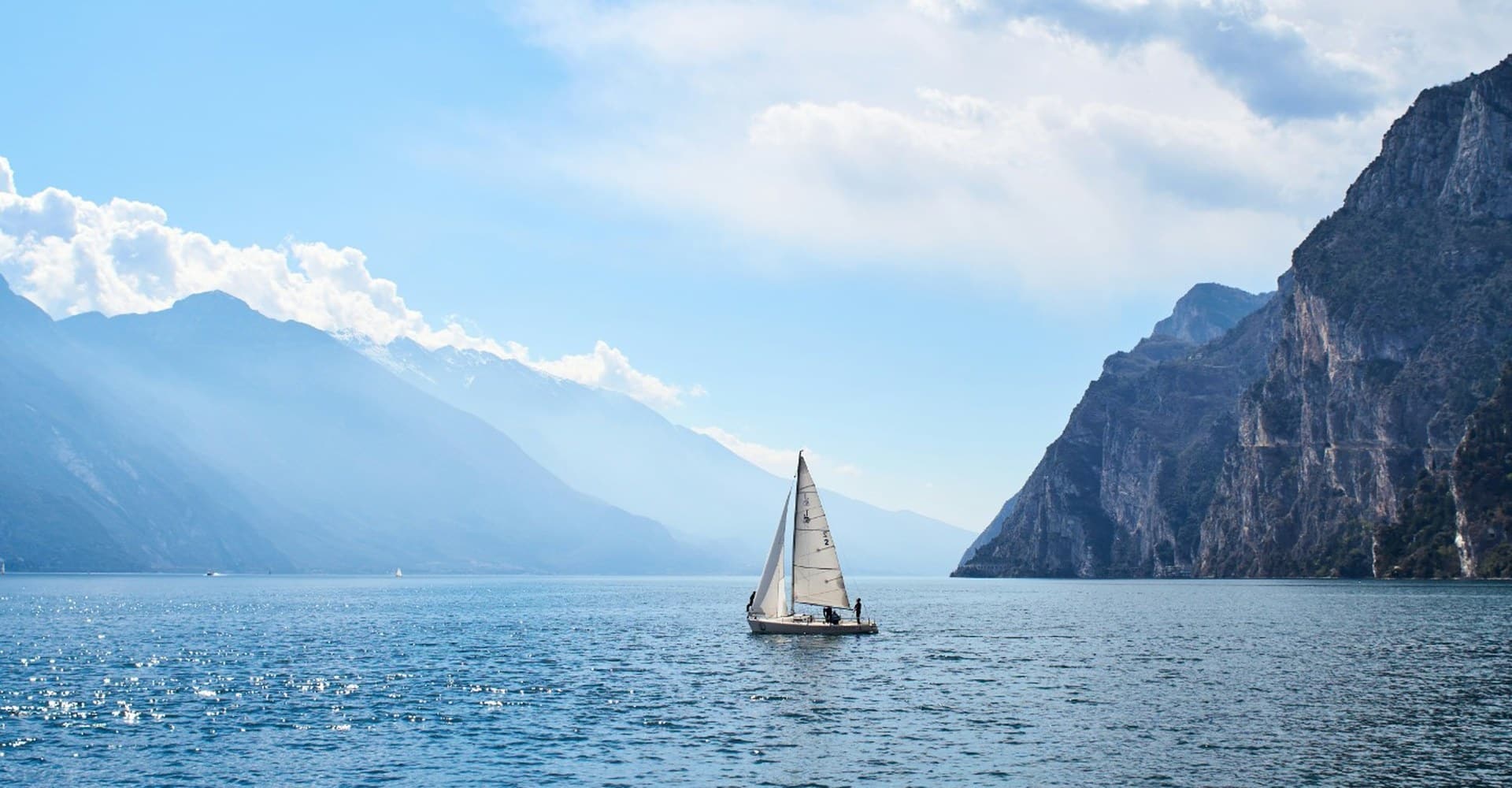 Barca a vela sul Lago di Garda tra montagne e luce del pomeriggio.